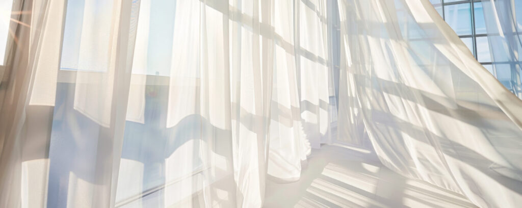 gallery Light streams through sheer white curtains blowing gently in the wind, highlighting window panes.