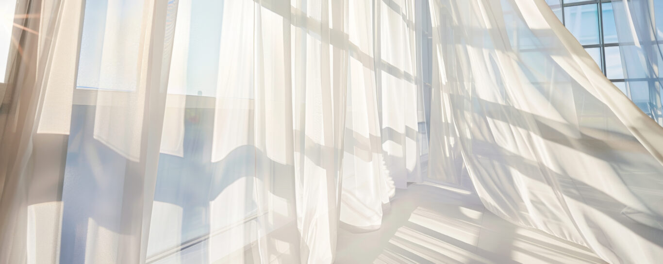 Gallery Light streams through sheer white curtains blowing gently in the wind, highlighting window panes.