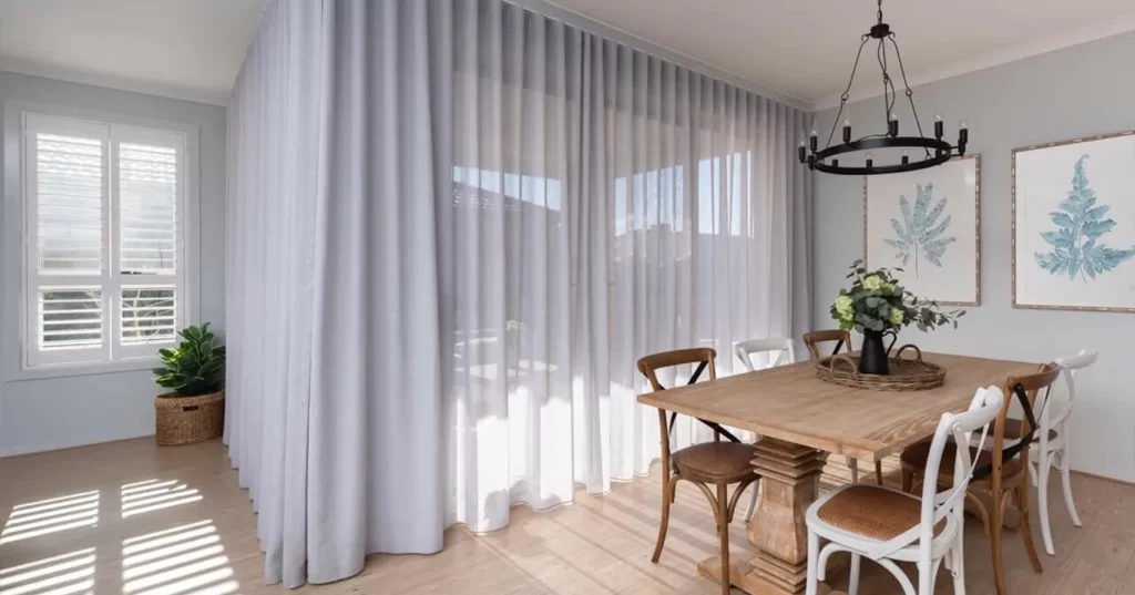 gallery The dining area features a light brown wooden table with four light brown, and four white, cross-back chairs.