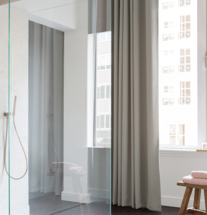Gallery Modern bathroom with walk-in glass shower, large window, gray curtains, wooden stool, and pink towels.