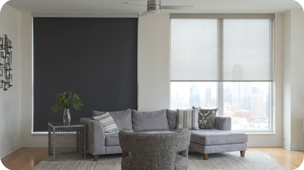 A blackout roller shade darkening one window next to a light-filtering roller shade glowing softly in a bright living room