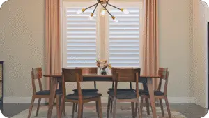 A Dallas dining room dressed with white plantation shutters and floor-length drapery
