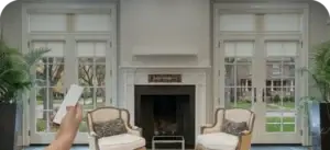 Handheld remote lowering four motorized roller shades in a bright living room
